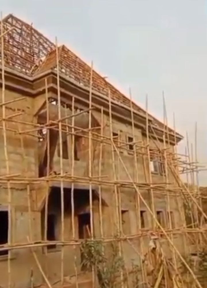 N-SOL Construction managing building project in Opi, Nsukka, Enugu State, showing two-storey carcass blockwork and timber roof truss framework under construction with perimeter scaffolding.